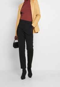 Musta räätälöity housut, viininpunainen pooloneule ja keltainen bleiseri. Yhdistetty mustiin nilkkureihin ja pieneen teksturoituun mustaan käsilaukkuun.