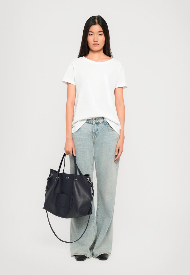 Hvit t-skjorte med korte ermer, lyseblå høytlivsjeans og en marineblå skinnveske med sølvfittings og en frontlomme.