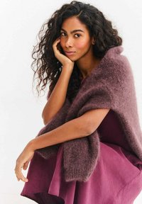 Pluszowy, ciemny szal w kolorze mauve narzucony na głęboką śliwkową sukienkę. Miękka, puszysta faktura, luźny krój i szerokie rękawy, które zwiększają ciepło i komfort.
