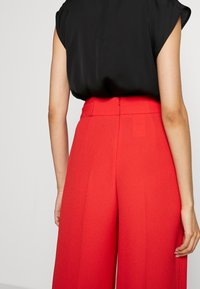 Černé tričko s krátkými rukávy, spárované s vysokými širokými červenými kalhotami s zadním zipem a hladkým povrchem.