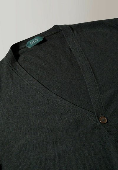 Gilet noir à col en V fabriqué en tissu doux, présentant un unique bouton marron et une couture détaillée le long des bords.