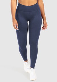 Marina högmidjade leggings gjorda av slät, elastisk material med ribbad midja och texturerade detaljer längs låren. Bärs med vita sneakers.