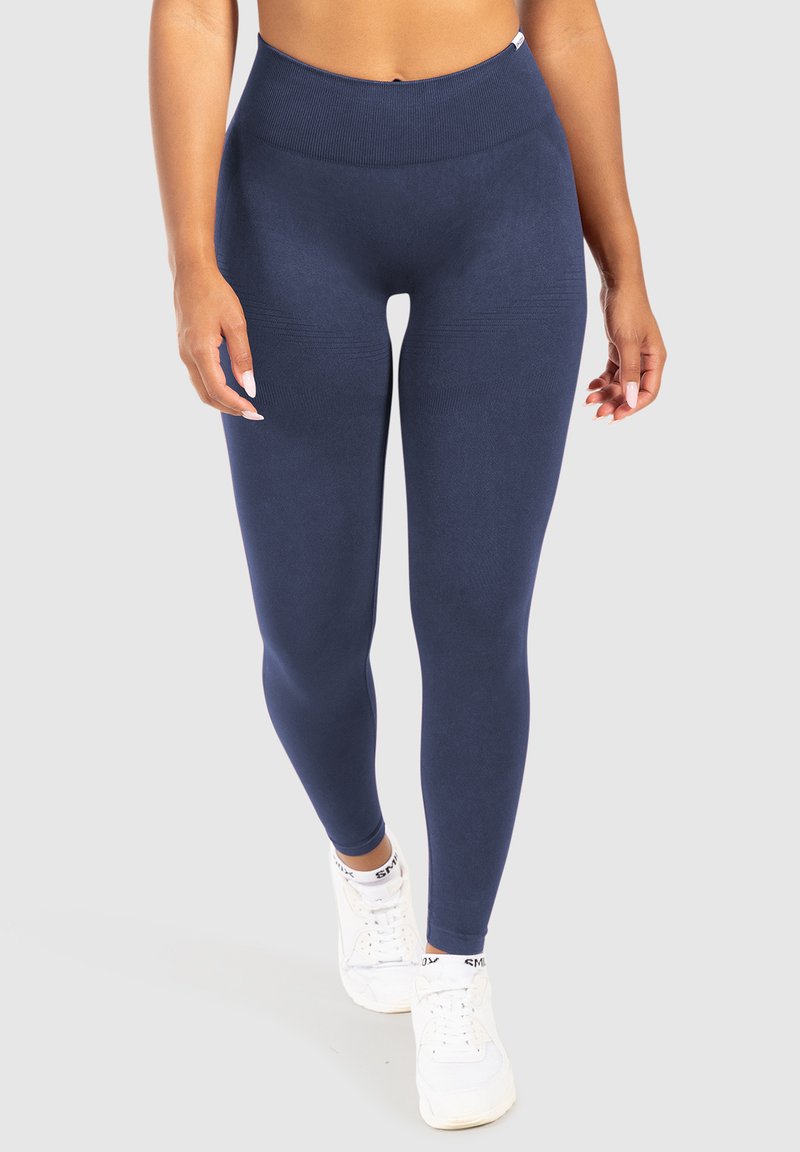 Marina högmidjade leggings gjorda av slät, elastisk material med ribbad midja och texturerade detaljer längs låren. Bärs med vita sneakers.