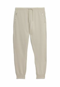 Beige joggerbukser lavet af blødt stof, med elastisk talje, sidelommer med lynlås og tætsiddende manchetter ved anklerne.
