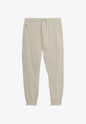 Beige joggerbukser lavet af blødt stof, med elastisk talje, sidelommer med lynlås og tætsiddende manchetter ved anklerne.