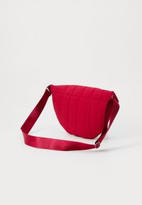 Borsa a spalla rossa trapuntata con forma arrotondata, dotata di una larga tracolla in tessuto e superficie testurizzata. La chiusura non è visibile.