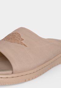 Μπεζ σανδάλι slide με ανοιχτά δάχτυλα, με ανάγλυφο λογότυπο Air Jordan φτερό στο λουράκι και υφή στη σόλα για καλύτερη πρόσφυση.