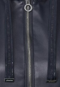 Mörkblå läderjacka med en silverfärgad dragkedja med ett runt drag och märkt dragkedjetape. Texturerad yta med subtilt skimmer.