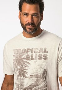 Camiseta de manga corta de color claro con un gráfico de "Tropical Bliss" que presenta palmeras y un diseño costero en tonos marrones. Textura suave, corte clásico.