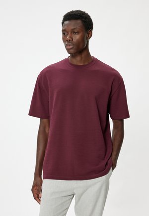 Bordeaux, t-shirt met korte mouwen en ronde hals, gemaakt van een textuurstof met een comfortabele pasvorm. Het model draagt lichtgekleurde broeken.