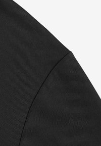 Zbliżenie na teksturowaną czarną tkaninę, ukazujące detal szwu i przeszyć rękawa odzieży.