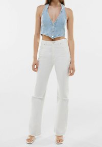Světlomodrý denimový cropped top s hlubokým V-výstřihem a knoflíkovým zapínáním, kombinovaný s bílými vysokými džínami s nestřiženým lemem. Průhledné sandály.