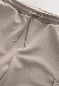 Pantaloni della tuta in cotone morbido di colore grigio chiaro, con vita elasticizzata, coulisse e tasca laterale. Texture liscia, design casual.