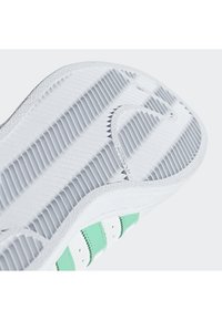 Semelle de sneaker blanche avec une texture nervurée, ornée de rayures vert menthe et de perforations. Conçue pour la traction et la flexibilité.