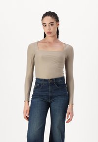 Beige Langarm-Body mit quadratischem Ausschnitt, kombiniert mit hoch taillierten, dunkelblauen weiten Jeans. Glatte Textur, enganliegendes Design.