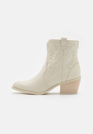 Ankelcowboystøvle i cremefarve med broderet dekorativt mønster og stablet træblokhæl, set fra siden på hvid baggrund.