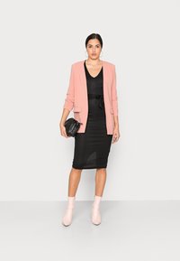 Blazer rosa claro sobre um vestido preto justo com um cinto, combinado com botas de tornozelo rosa pálido. Clutch preta simples na mão.