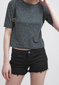 Šedá košile s krátkým rukávem a texturovaným povrchem spojená s těsnými černými denimovými šortkami s jemným krajkovým lemem na spodním okraji. Viditelné černé ramenní popruhy.