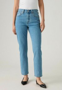 Jeans de tiro alto en denim de color azul claro, con un diseño de pierna recta. Cuenta con un cierre de botón en la parte delantera, cinco bolsillos y un acabado desgastado.