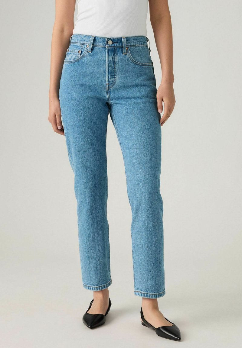 Jeans de tiro alto en denim de color azul claro, con un diseño de pierna recta. Cuenta con un cierre de botón en la parte delantera, cinco bolsillos y un acabado desgastado.