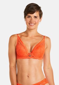 Soutien-gorge en dentelle orange avec une forme triangulaire, des bords festonnés et un fermoir décoratif au centre. Présente des motifs complexes sur toute sa surface.