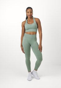 Conjunto de sujetador deportivo y leggings verdes sin costuras, con cintura alta, textura acanalada y tejido elástico ligero. Combinado con zapatillas deportivas blancas.