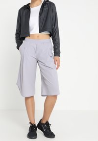 Chaqueta negra corta de Nike, top corto blanco y pantalones cortos gris claro hasta la rodilla. Los pantalones cortos tienen bolsillos y logo, combinados con zapatillas negras.
