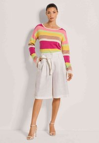 Gestreepte trui in tinten roze, geel en beige; gecombineerd met hoge linnen shorts in lichtbeige met een strikdetail in de taille.