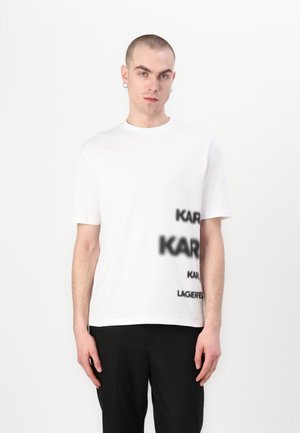 T-shirt en coton blanc avec un texte noir à pois lisant "KARL" et "LAGERFELD" dans un design graphique audacieux. Manches courtes et col rond.