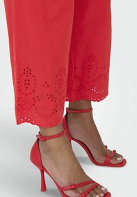 Rode, geborduurde cropped broeken met een scalloped zoom en ronde uitsparingen. Gecombineerd met rode sandalen met hoge hakken en straps.