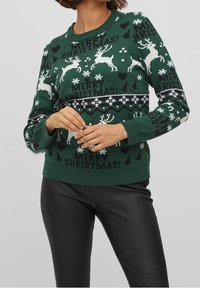 Grön jultröja med vita renar, snöflingor och texten "GOD JUL!" Ribbstickade ärmslut och nederkant; mjukt stickat material.