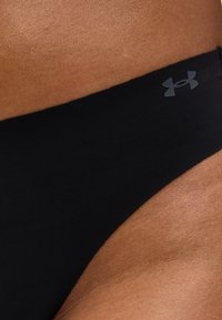 Κοντινό πλάνο μέσης ατόμου που φοράει μαύρα αθλητικά σορτς Under Armour με ορατό λογότυπο στη ζώνη μέσης.