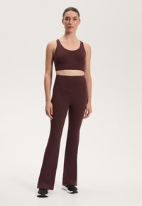 Burgundy sportmelltartó és bővülő leggings rugalmas anyagból. A melltartón kivágott rész található; a leggings sima felületű.