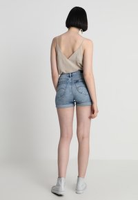 Beige v-ringad linne med tunna axelband kombinerat med ljusblå denimshorts. Vita ankelboots kompletterar outfiten. Mjuka texturer genomgående.