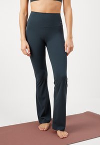 Ciemnoniebieskie legginsy sportowe z wysokim stanem, wykonane z elastycznego materiału, zaprojektowane z myślą o komforcie i swobodzie ruchów, wystawione na macie do jogi.