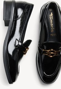 Mocassini in pelle verniciata nera con tacco basso a blocco e dettaglio in hardware dorato. Presentano una punta arrotondata e sottili accenti di cucitura.