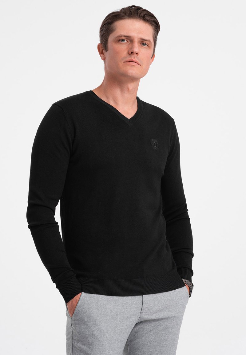 Schwarzer, langärmeliger Strickpullover mit V-Ausschnitt und gerippten Bündchen, der ein dezentes Logodetail auf der Brust aufweist. Weicher Stoff und klassischer Schnitt.