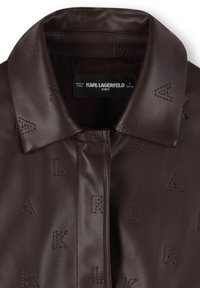 Giacca in pelle marrone con colletto strutturato. Presenta un motivo in rilievo "KARL". Tessuto liscio, chiusura centrale con zip e etichetta visibile.