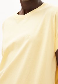 Cotton t-shirt in light yellow with a soft texture, round neckline, and short sleeves. Features a small embroidered logo on the chest.