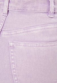 Fialová deninová látka zobrazující detailní záběr kapsy s viditelnými švy a hladkou texturou. Obsahuje klasický design s pěti kapsami.