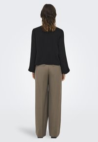 Un haut noir à manches longues avec une coupe décontractée, associé à un pantalon large marron clair avec des poches arrière et une texture lisse.