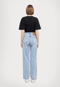 T-shirt nera in cotone a maniche corte, abbinata a jeans chiari a vita alta con una patch in pelle sul retro.