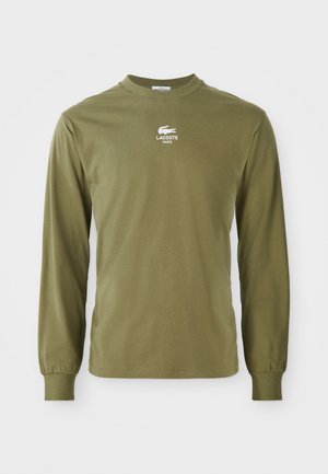 Olivgrön långärmad skjorta med rund halsringning, med en liten vit Lacoste-logga och texten "LACOSTE PARIS" centrerad på bröstet.