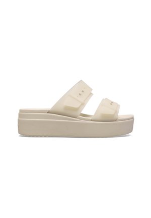 Beige Plateau-Slide-Sandale mit zwei breiten Riemen, die verstellbare Schnallen haben, und einer dicken Sohle, von der Seite vor weißem Hintergrund gezeigt.