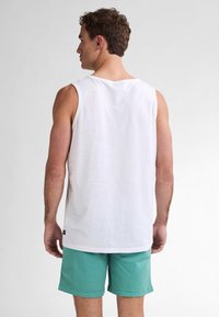 Camicetta bianca in cotone senza maniche con una vestibilità rilassata, abbinata a pantaloni corti color teal. Design minimalista, texture morbida e senza ulteriori motivi.