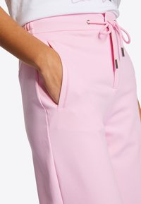 Lichtroze joggingbroek met elastische tailleband en trekkoord, voorzien van zijzakken en een gladde, zachte textuur. Minimalistisch ontwerp.