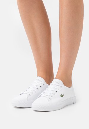 White lace-up sneakers made of smooth synthetic material, featuring a rubber sole and a green embroidered crocodile logo on the side.