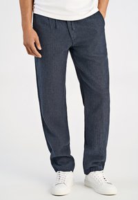 Ciemnoniebieskie, teksturowane spodnie o luźnym kroju, z elastycznym paskiem w talii i mankietami. Noszone z białymi trampkami i gładką koszulką.