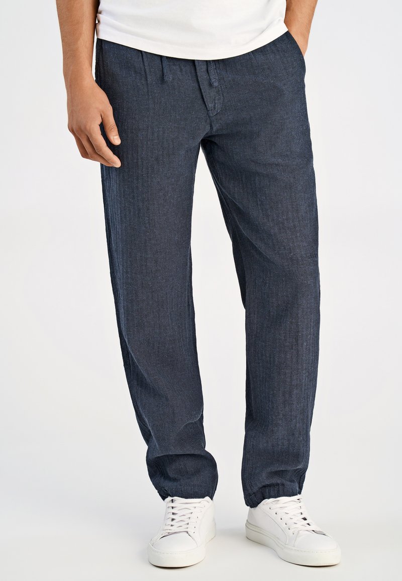 Ciemnoniebieskie, teksturowane spodnie o luźnym kroju, z elastycznym paskiem w talii i mankietami. Noszone z białymi trampkami i gładką koszulką.