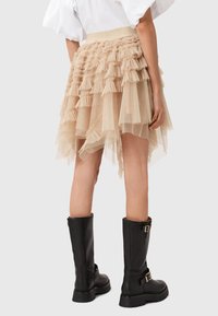 Gonna in tulle beige con rouches a strati, orlo asimmetrico e ampia cintura elastica, abbinata a stivali neri al ginocchio.